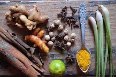 Natural ingredients used in JAMU ORGANIC HERBAL including ginger, turmeric, cinnamon, and lemongrass displayed on a wooden surface.