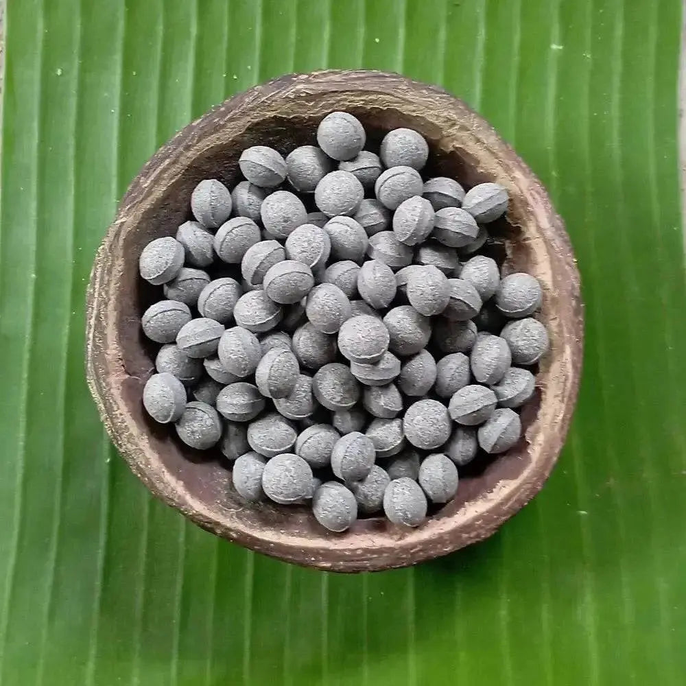 Natural butterfly pea flower supplement tablets in a bowl on a green leaf background.