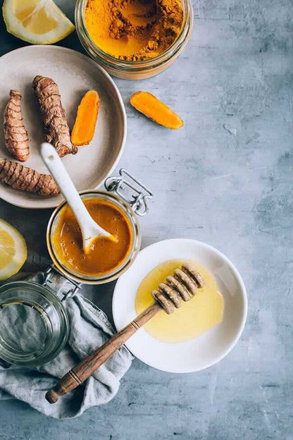 Herbal ingredients with turmeric, ginger, honey, and lemon on a grey surface, showcasing natural elements of JAMU ORGANIC HERBAL.